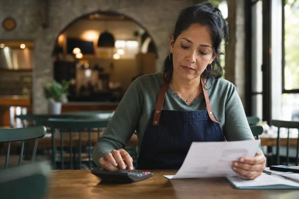 Dueña de un café revisa una oferta de préstamo con una calculadora después de cerrar