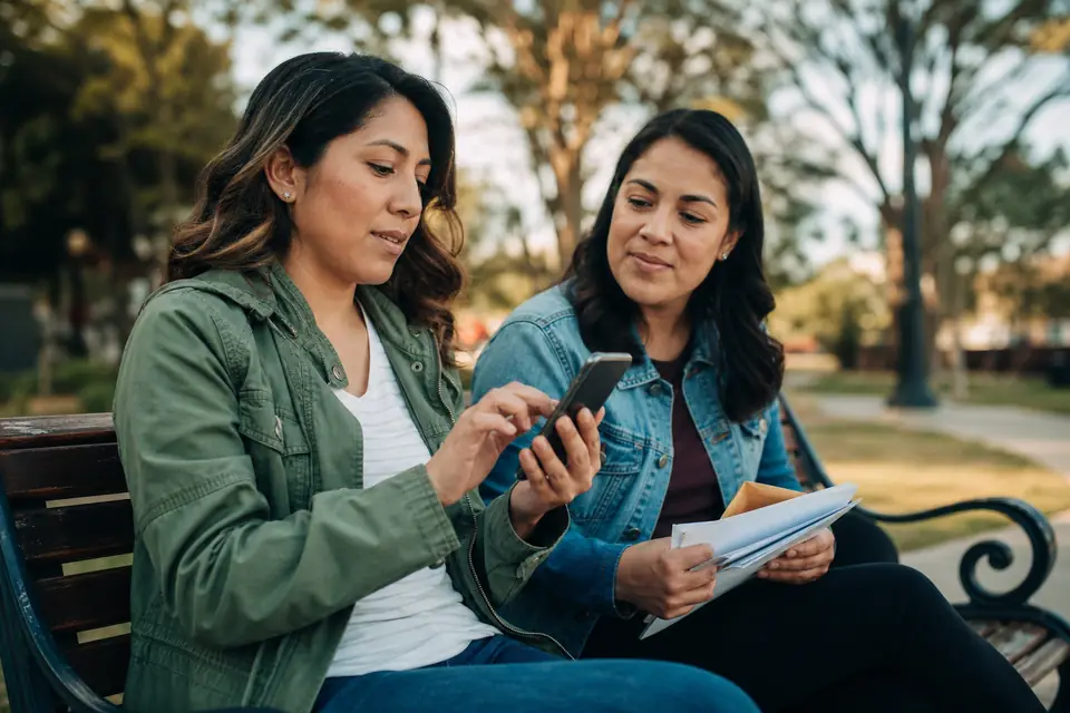 Dos personas en banco del parque activando pagos automáticos con sobres al lado